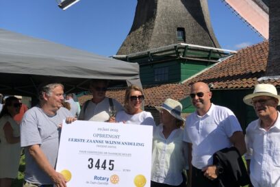 Fotobijschrift:Overhandiging van de cheque bij De Schoolmeester door voorzitter Pleunie Florijn van RC De Zaan-Zaandijk (midden met hoed) aan molenaar André Koopal van molen Het Pink (uiterst links).